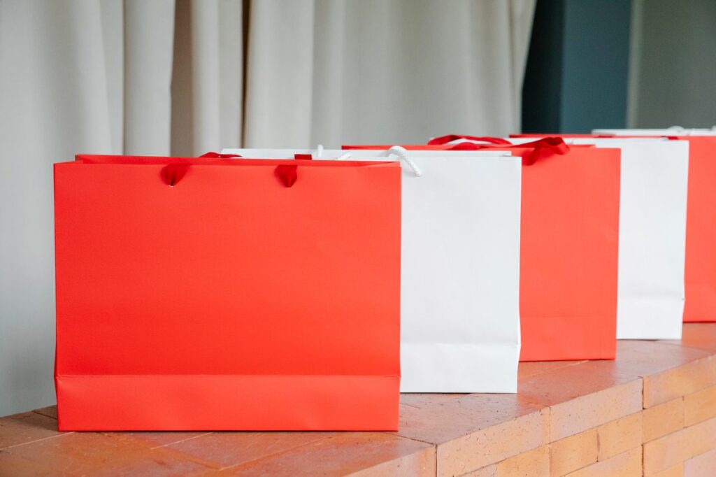 pexels photo 7319110 Set of red and white paper shopping bags placed on brick shelf in studio